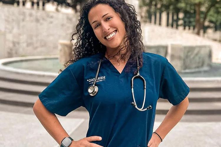 Herzing online BSN student in blue scrubs smiling with hands on hips in courtyard